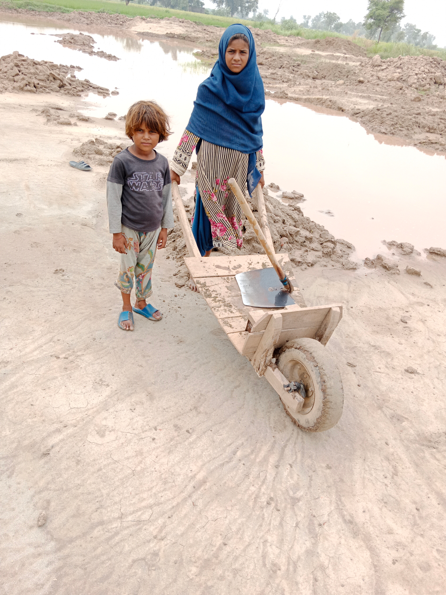 A young girl and a small child at a brick kiln site in rural Pakistan, pushing a wooden cart
