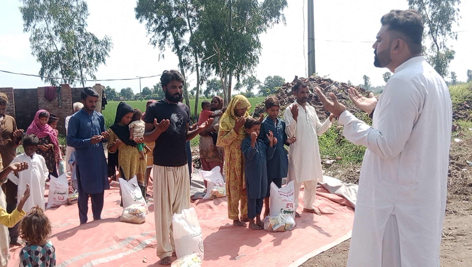 Pastor Shahzad Rafaqat praying with brick kiln families beside their monthly grocery sacks after the floods in Pakistan