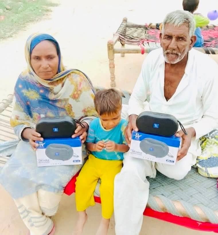 Two elderly women holding Audio Bible players outside a brick home